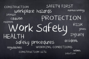 Chalkboard-style word collage centred around 'Work Safety', with related terms such as 'SAFETY FIRST', 'HAZARDS', 'PROTECTION', 'HEALTH', 'INJURY', 'REGULATIONS', 'HELMET', and 'CONSTRUCTION SITE' written in various sizes and styles.