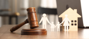 Wooden judge's gavel beside cutout figures of a family and a house, symbolising family law, custody, or property settlement decisions.