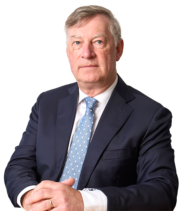Professional portrait of Val Stone, he is wearing a dark navy suit, a white shirt, and a light blue tie featuring a white polka dot pattern. He is sitting with his hands clasped in front of him, with a gold wedding ring visible