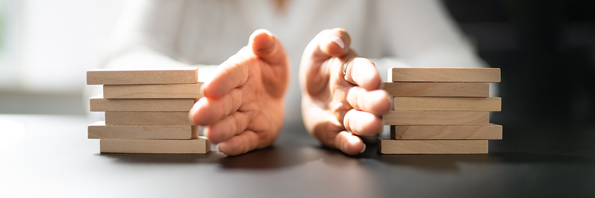 Close-up of two hands separating two equal stacks of wooden blocks on a table, symbolising division or distribution, possibly in a legal or financial context.