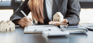 Real estate solicitor signing documents with wooden house models on desk, representing residential property legal services.